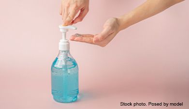 Hände die sich Desinfektionsmittel aus einem Seifenspender nehmen vor einem rosanem Hintergrund