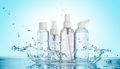 Vier Kosmetikflaschen mit Wasserspritzern drum herum vor einem blauen Hintergrund