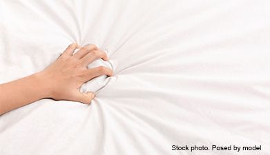 Eine Hand, die sich in ein weißes Bettlaken krallt