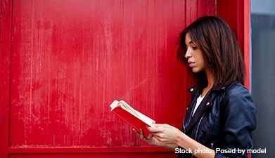 Eine Frau die seitlich vor einer roten Wand steht und ein Buch liest