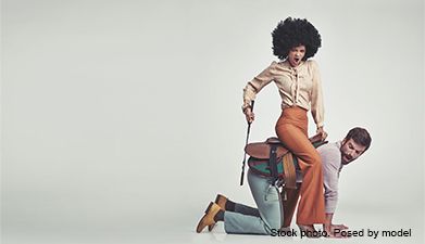 Eine Frau reitet auf einem Mann wie auf einem Pferd mit einer Gerte in der Hand