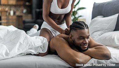 Eine Frau in weißer Unterwäsche sitzt auf dem Po eines Mannes, der im Bett liegt