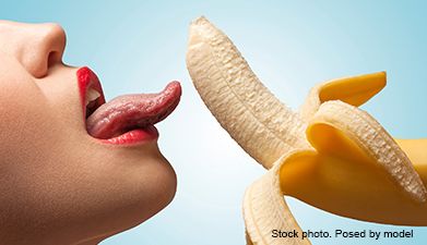 Eine Frau die ihre Zunge herausstreckt und fast an einer halb geschälten Banane leckt