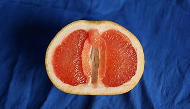 Eine aufgeschnittene Grapefruit, die wie eine Vulva aussieht vor einem blauen Hintergrund