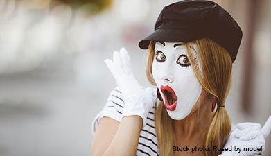 Eine Frau mit einem schwarzen Hut auf und weißen Handschuhen an, die wie ein Clown geschminkt ist un