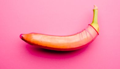Eine Banane die ein rotes Kondom übergezogen hat vor einem pinken Hintergrund