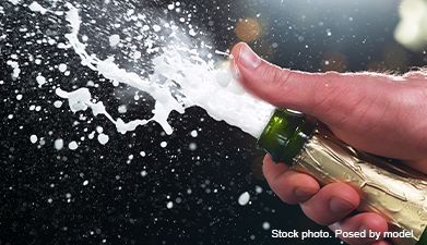 Eine Hand die eine Sektflasche hält aus der Sekt herausspritzt