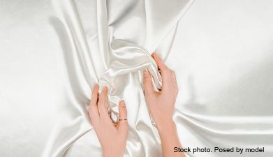 Zwei Hände die ein weißes in Falten gelegtes Satin Tuch halten