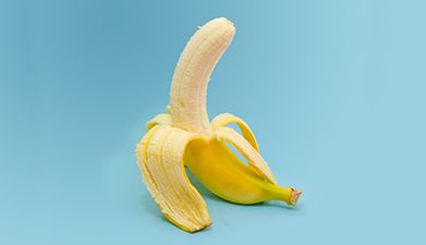 Eine halb geschälte Banane vor einem hellblauen Hintergrund