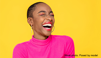 Eine lauthals lachende Frau in einem neonpinken Oberteil vor einem knallgelben Hintergrund