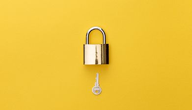 Ein Vorhängeschloss und ein Schlüssel vor einem gelben Hintergrund