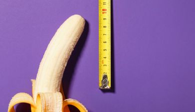 Eine halb geschälte Banane mit einem Zollstock daneben vor einem lila Hintergrund