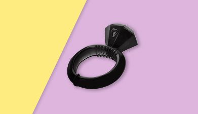 Schwarzer Penisring mit Diamant-Klitorisreizer auf gelb-lilanem Hintergrund