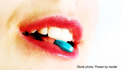 Eine Nahaufnahme eines halb geöffneten Mundes der eine Pille zwischen den Zähnen umfasst.