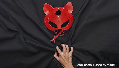 Eine rote BDSM Maske und eine Hand auf einem schwarzen Tuch