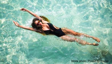Eine Frau die auf dem Rücken liegend in sexy Bademode im Pool schwimmt.