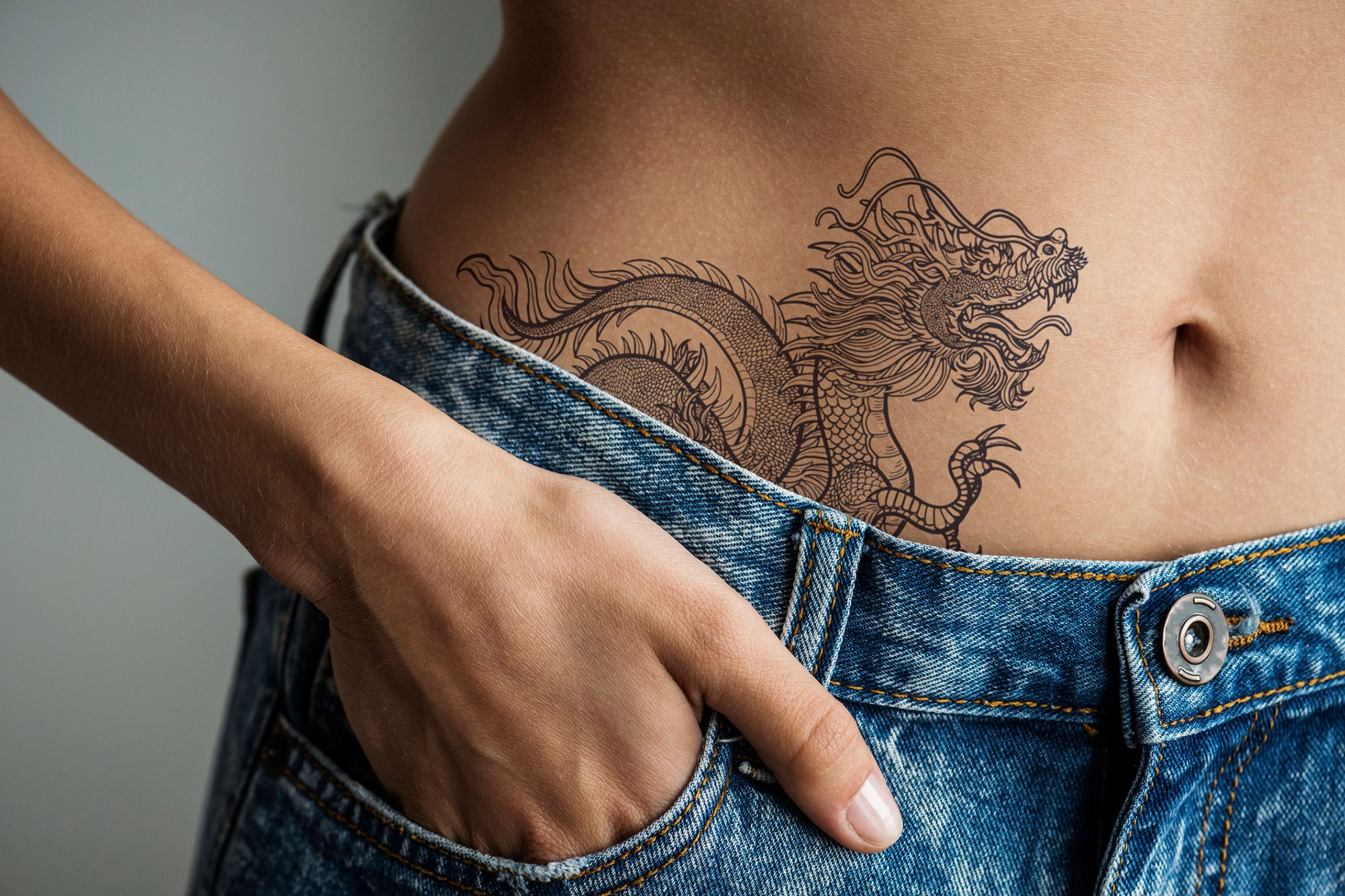 Eine Frau nur in Jeans bekleidet mit einem Tattoo im Bauch
