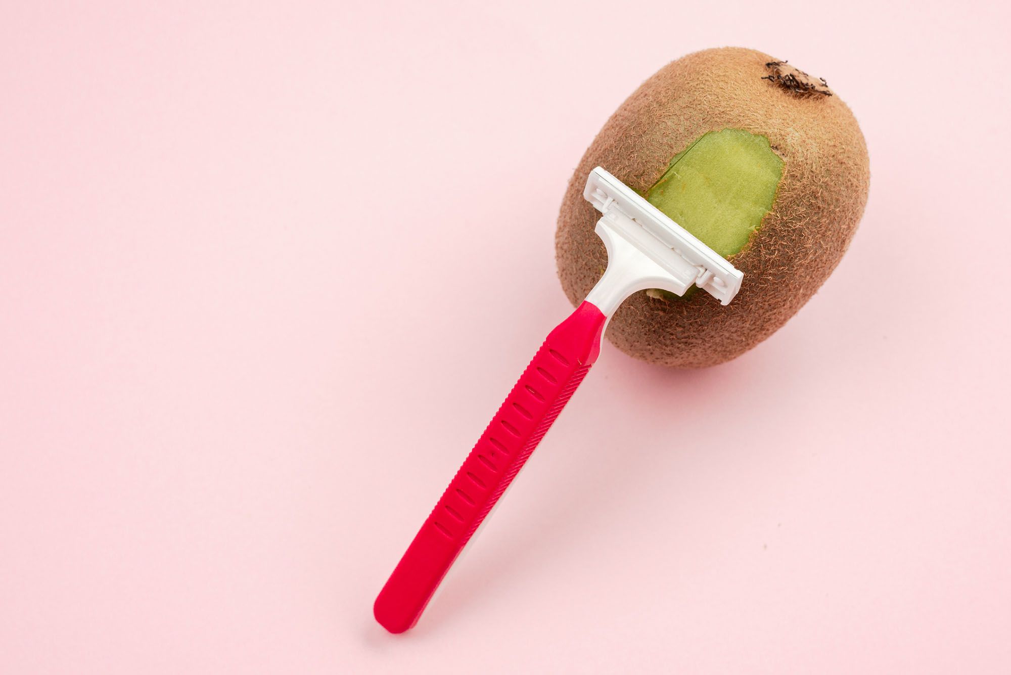 Kiwi, die rasiert wird auf rosanem Hintergrund