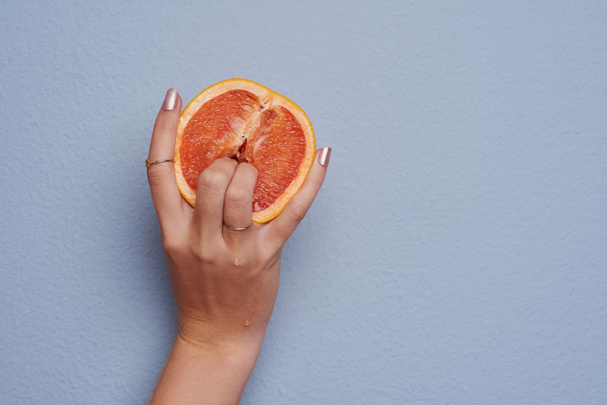 Zwei Finger, die eine Orange fingern auf grau-blauem Hintergrund