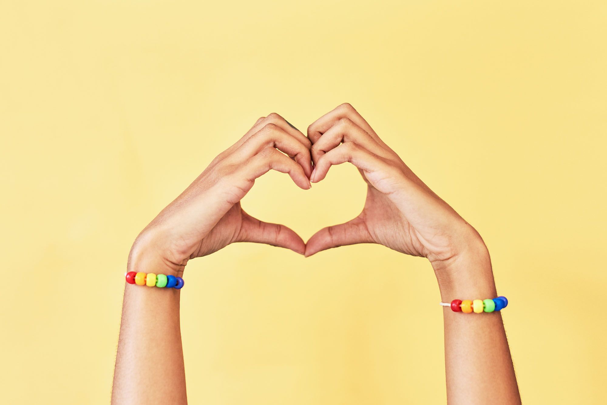 2 Hände mit Regenbogen-Armbändern formen ein Herz