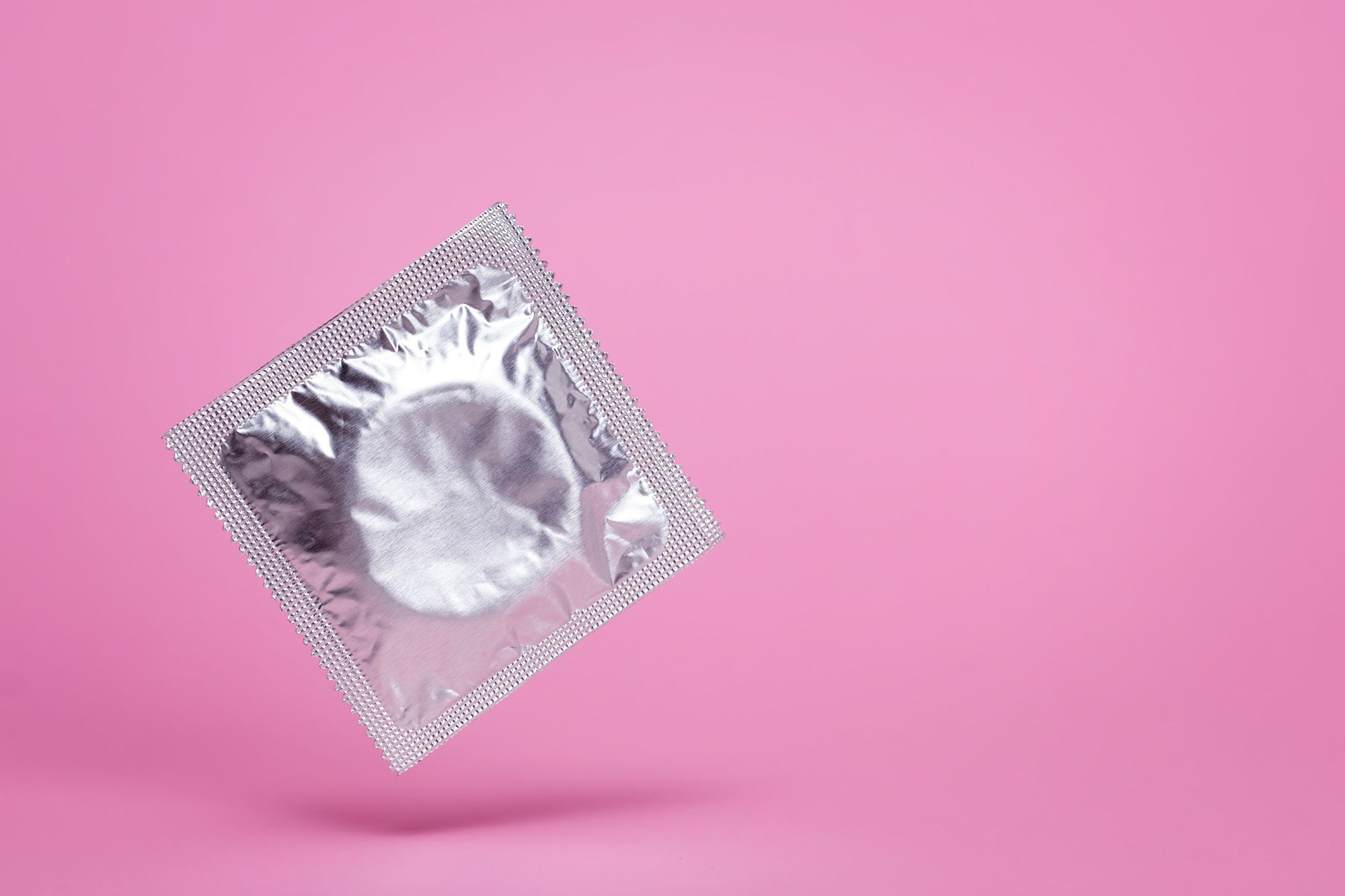 Silberne Kondomverpackung auf pinkem Hintergrund