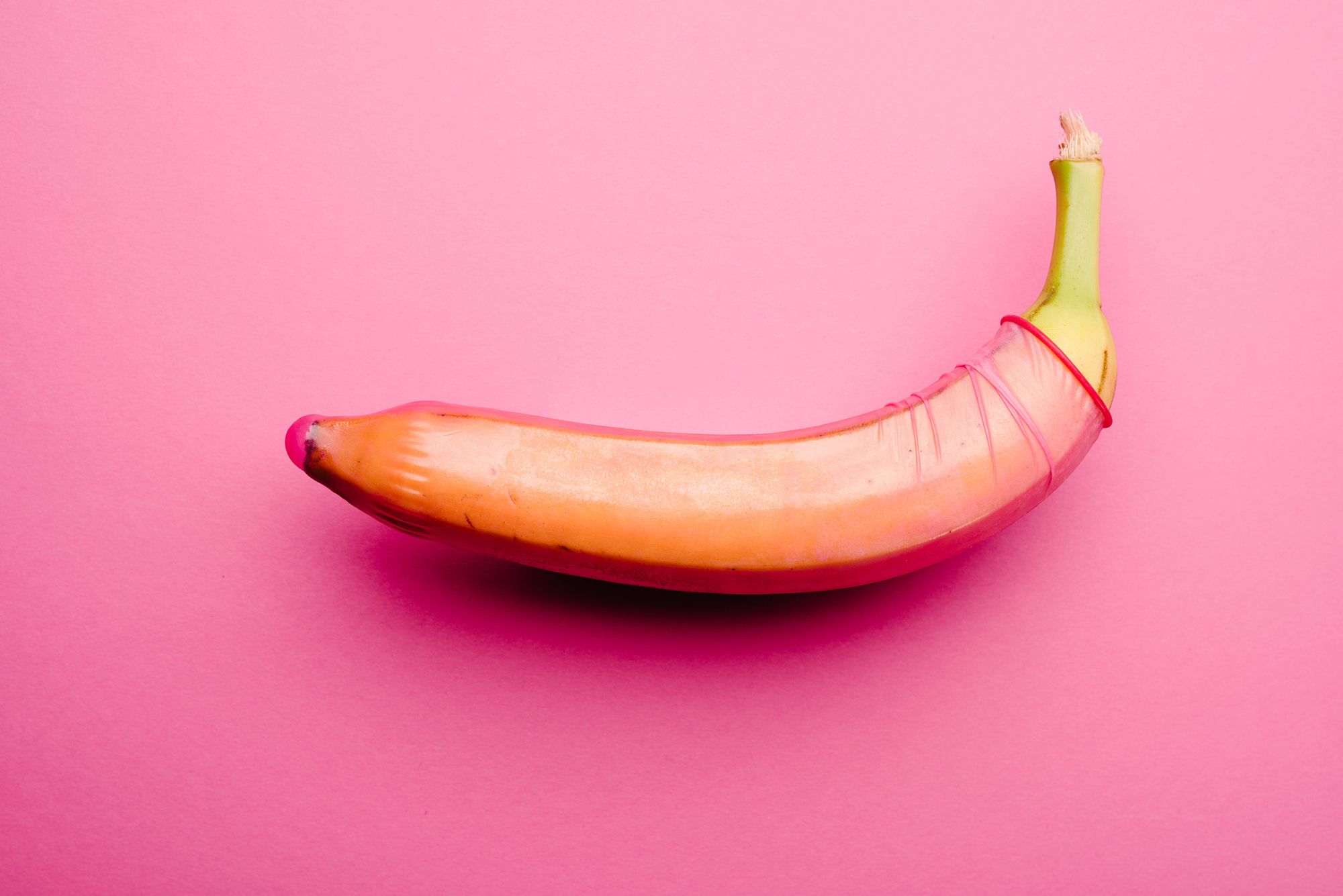 Banane mit rotem Kondom auf pinkem Hintergrund