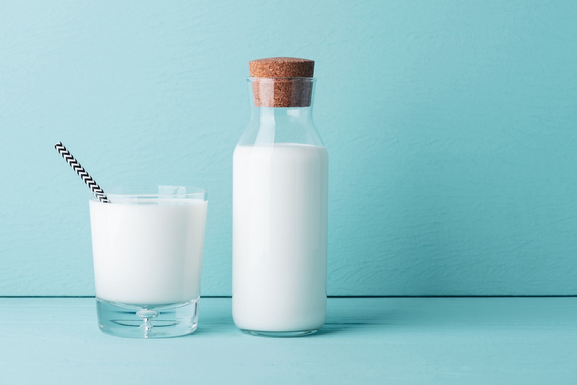 Ein Glas und eine Flasche Milch vor einem hellblauen Hintergrund