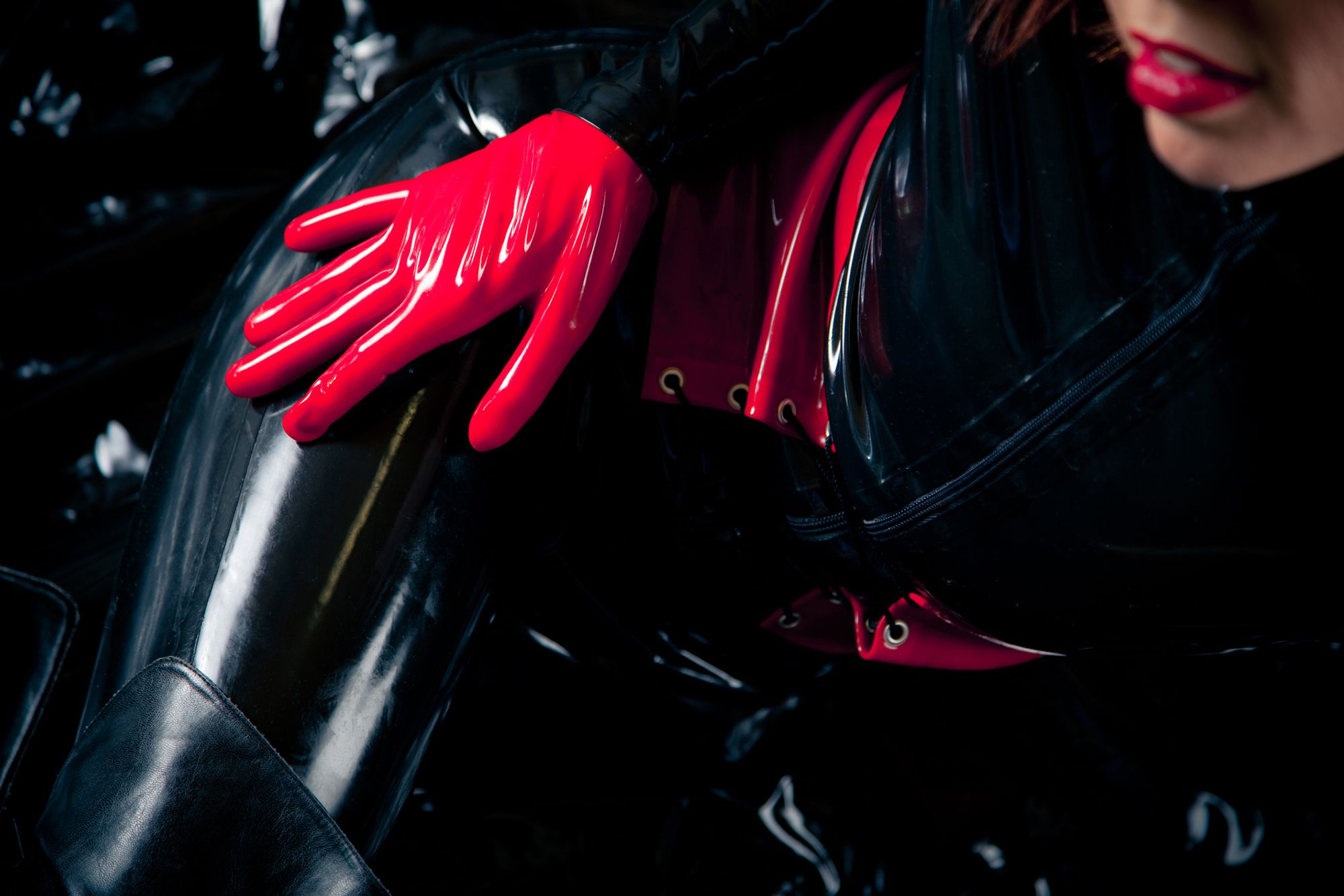 Eine Frau in schwarzer Lackkleidung mit roten Handschuhen und Lippen