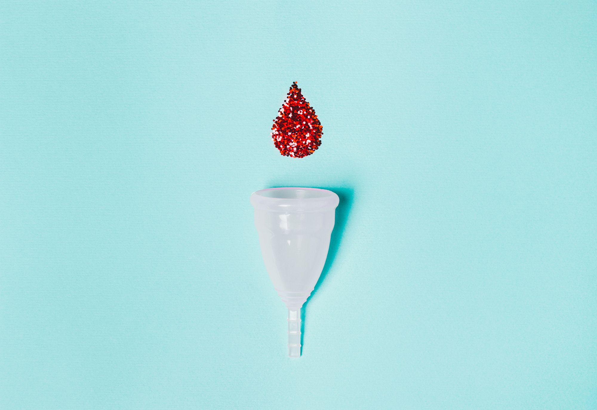 Menstruationstasse mit Blutstropfen aus Glitzer auf türkisem Hintergrund