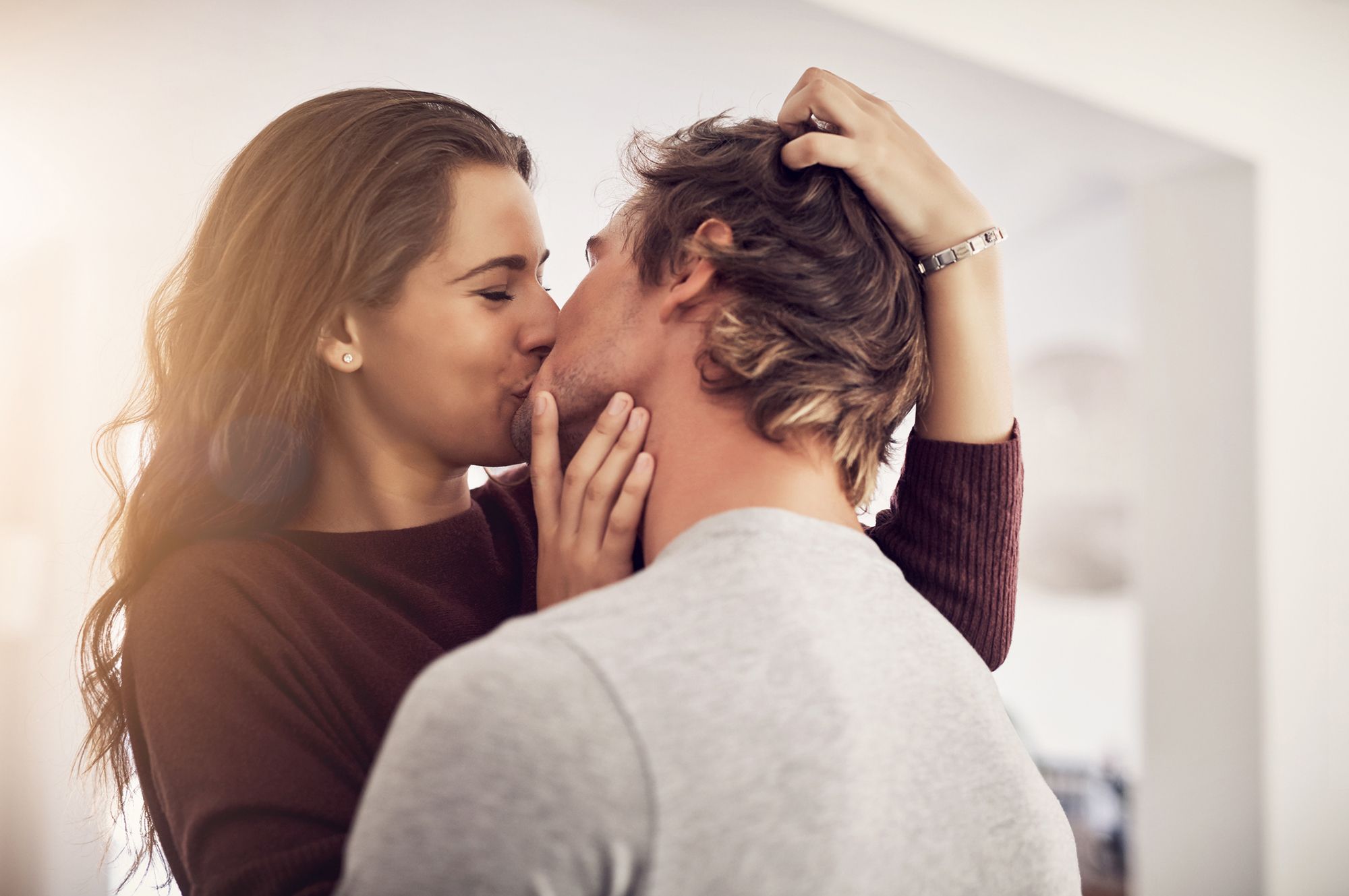 Brünette Frau in braunem Pullover und brünetter Mann in grauem Sweatshirt, die sich innig küssen