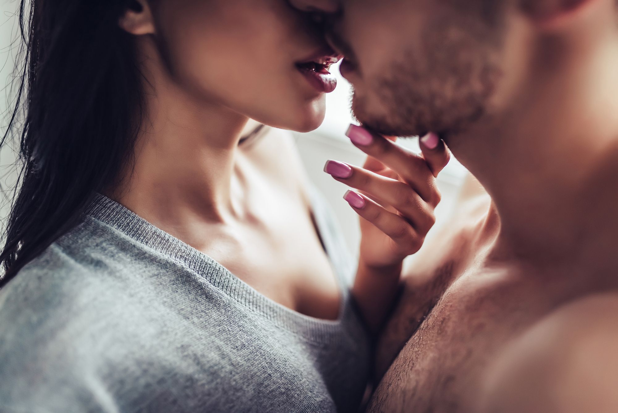 Schwarzhaarige Frau in grauem Shirt und mit pinken Fingernägeln und oberkörperfreier Mann, die sich sehr nahe kommen und beinahe küssen