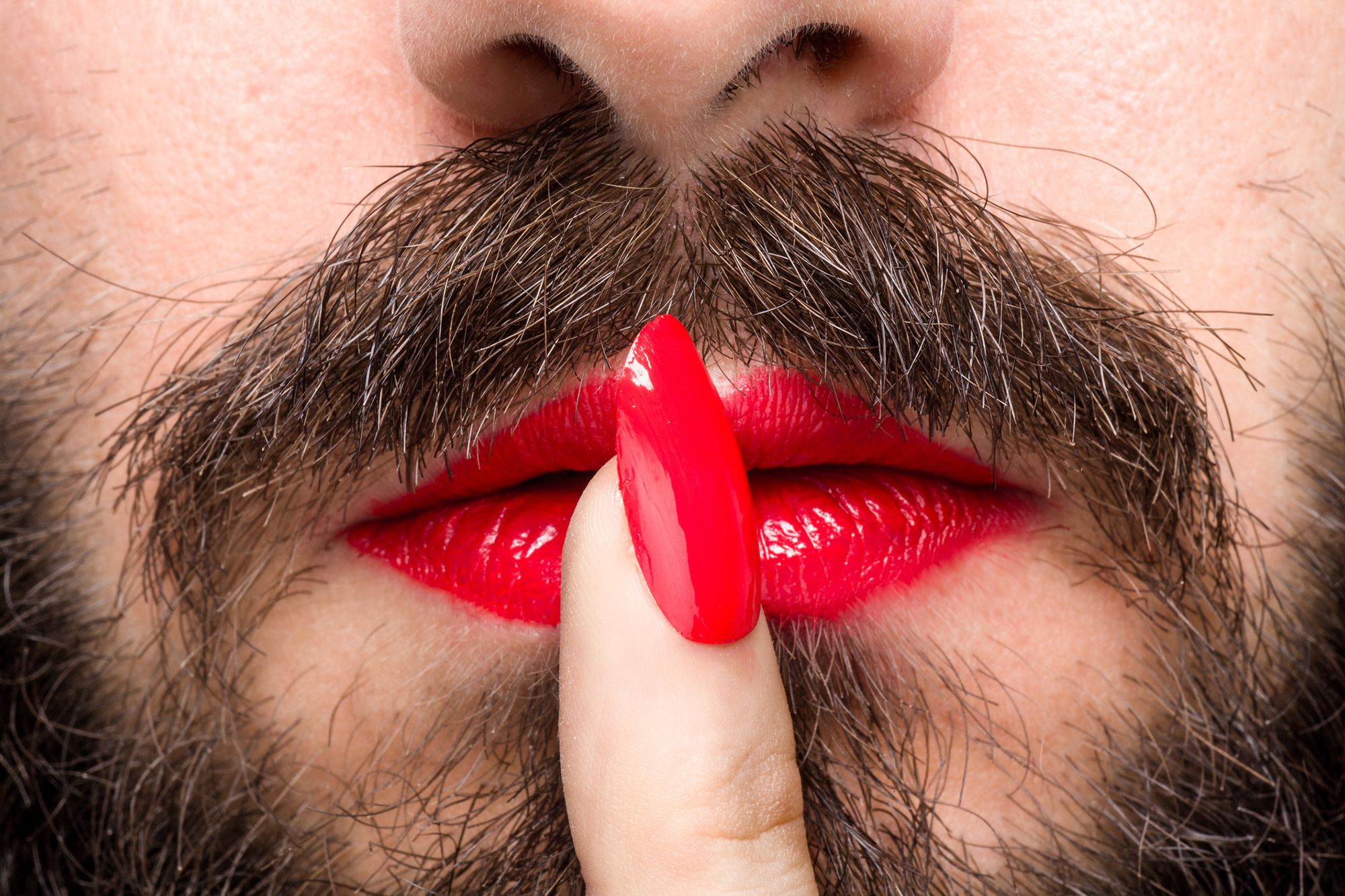 Mann mit Lippenstift und lackierten Fingernägeln macht ein Pssst-Zeichen
