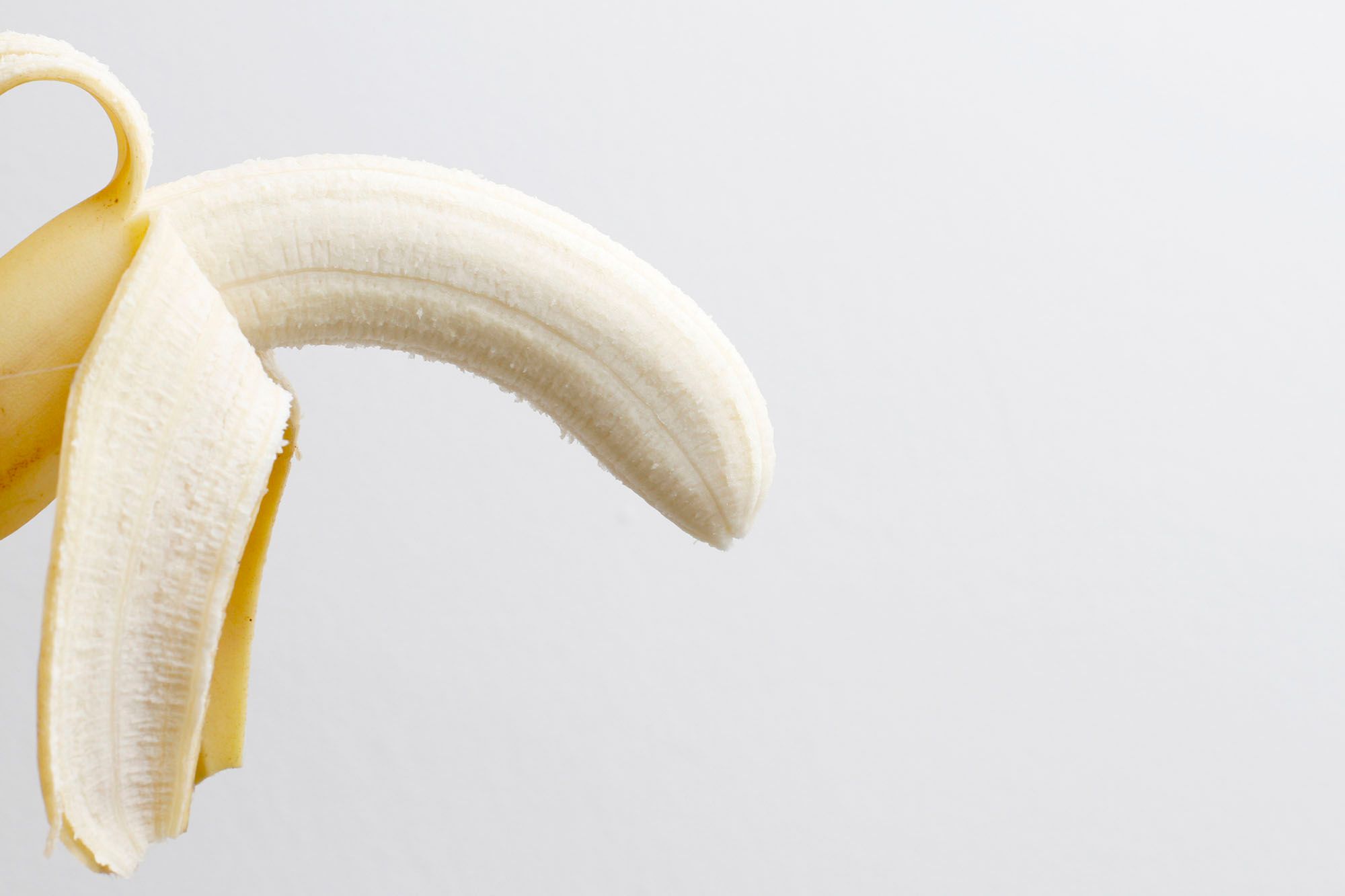 Halb geschälte Banane vor weißem Hintergrund
