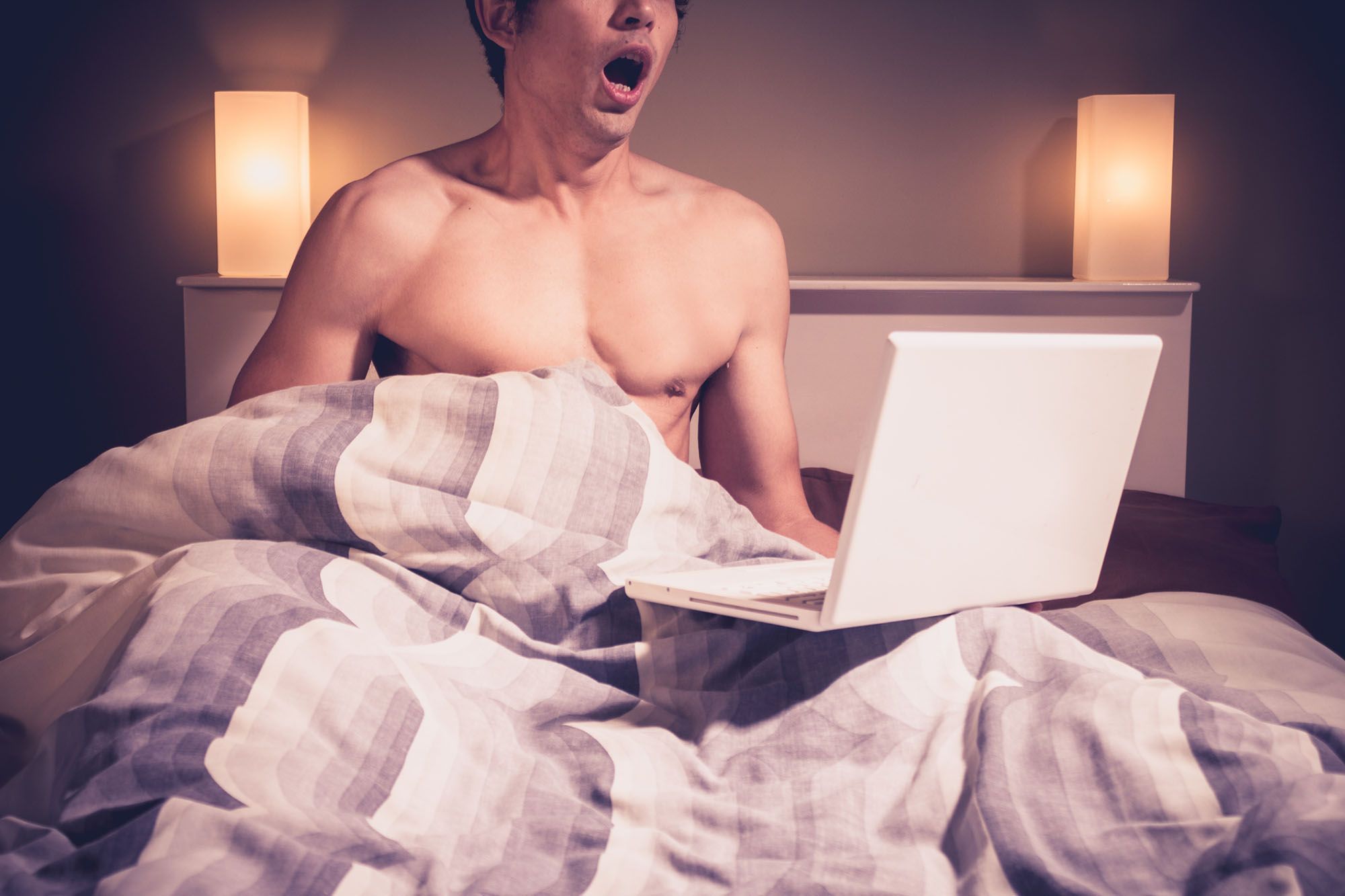 Mann, der sich im Bett vor einem Laptop einen runterholt