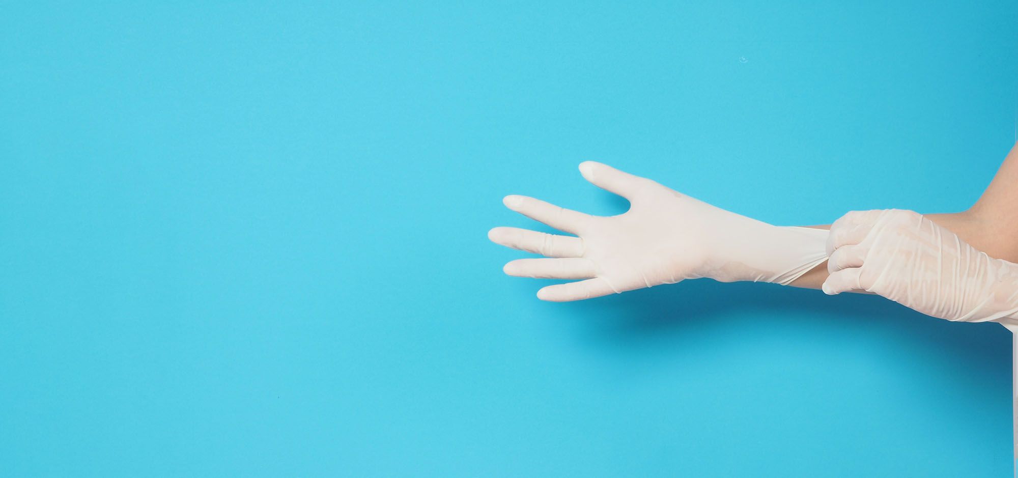Hände, die weiße Medizin-Handschuhe tragen vor hellblauem Hintergrund