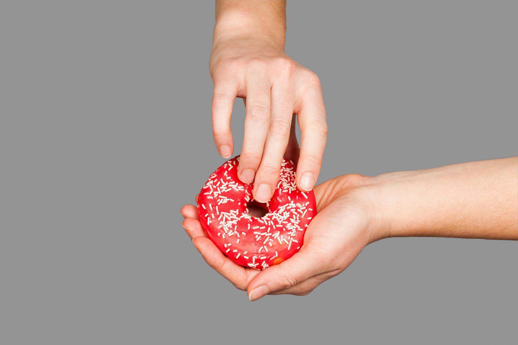 Zwei Hände, die einen Donut halten auf grauem Hintergrund