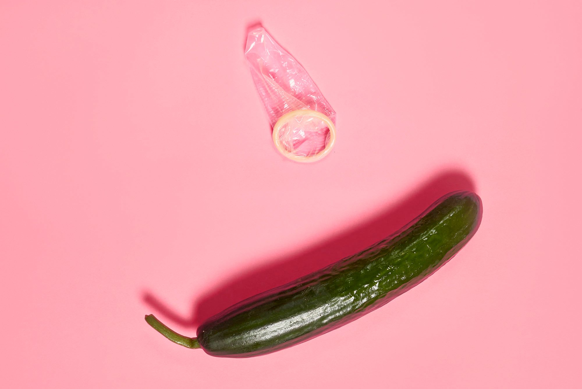 Gurke mit ausgepacktem Kondom auf pinkem Hintergrund