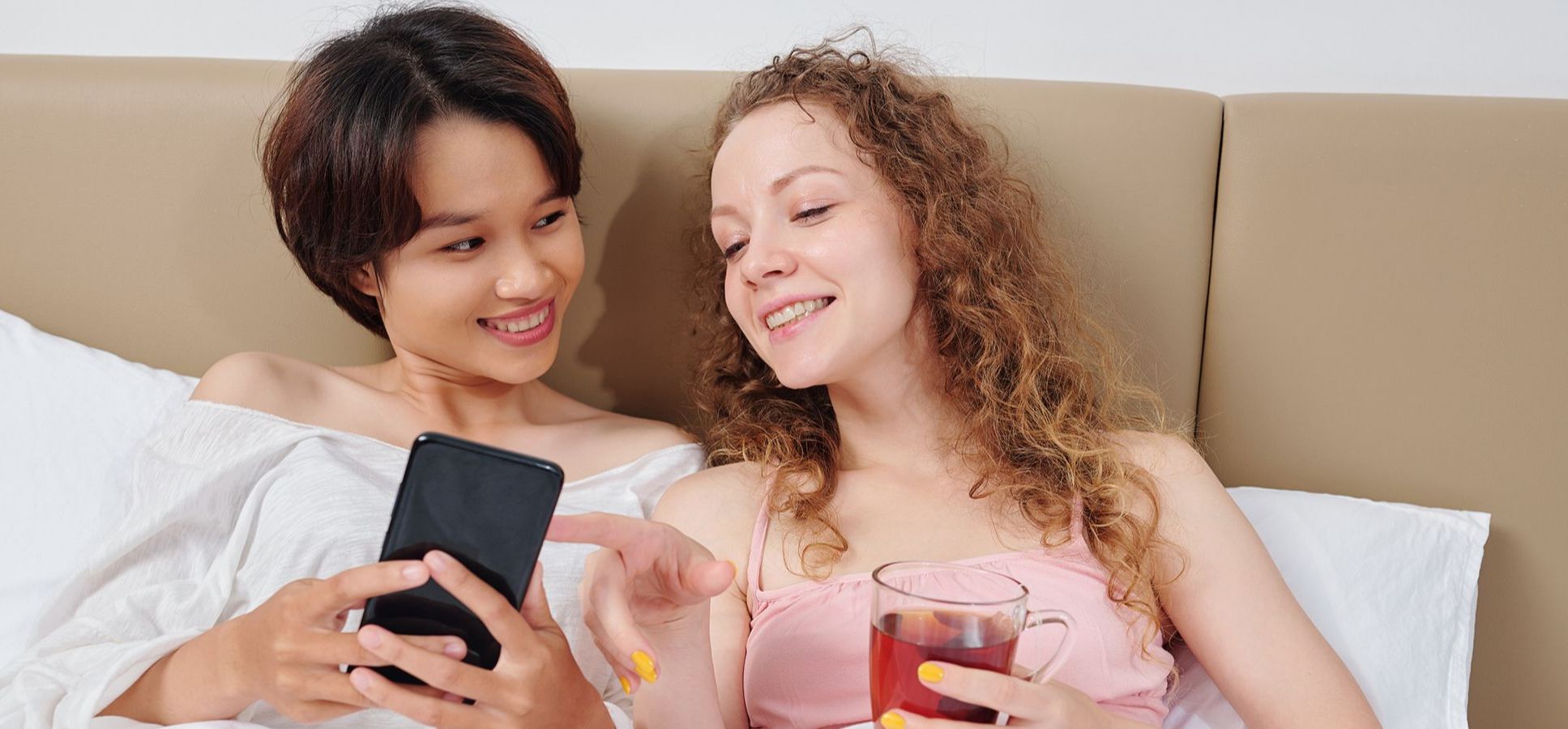 Paar liegt im Bett und sucht eine Sexspiele-App aus