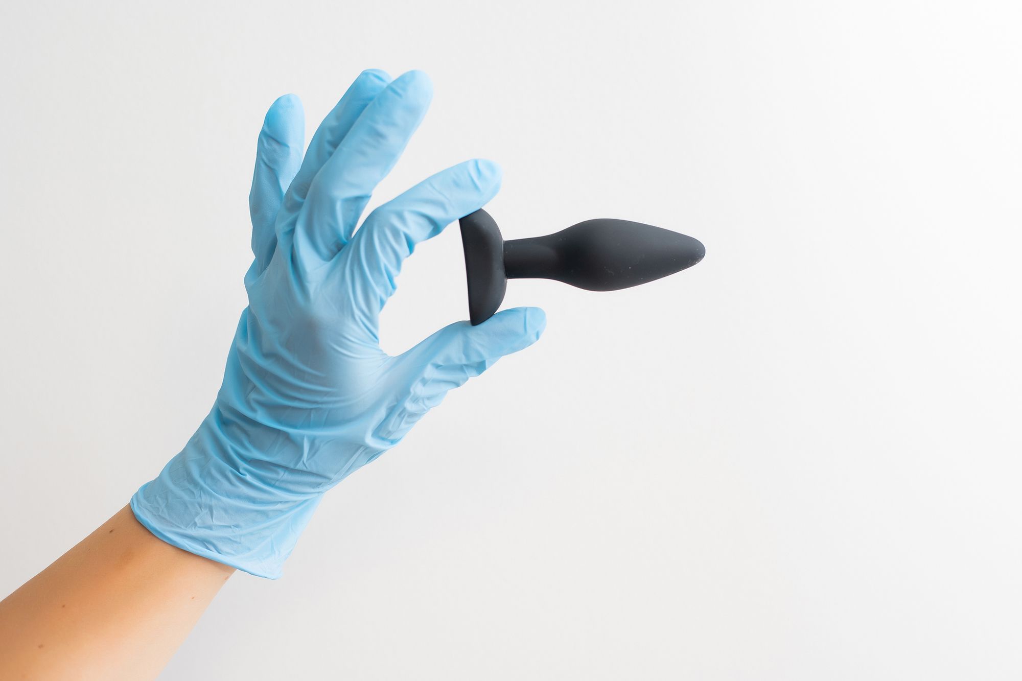 Hand im Latex-Handschuh hält einen schwarzen Analplug