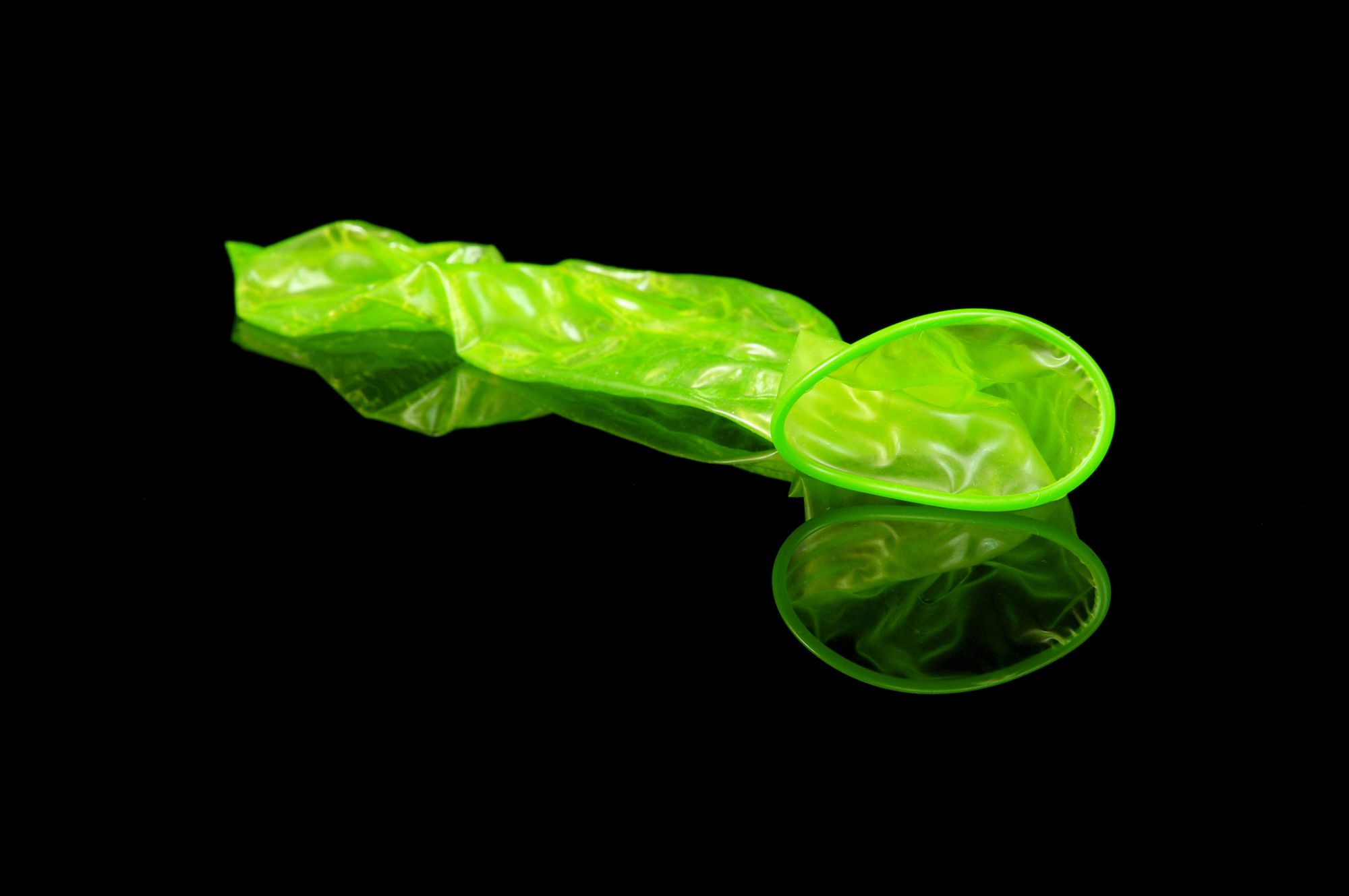 Abgestreiftes grünes Kondom auf schwarzem Hintergrund