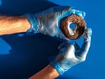 Männerhände mit blauen Handschuhen halten einen braunen Donut und schmieren diesen mit weißer Creme ein