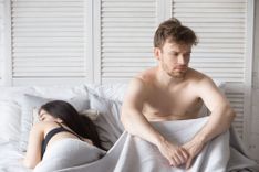 Mann sitzt nachdenklich im Bett, Frau liegt daneben