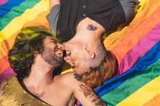 2 Männer liegen auf einer Regenbogenflagge und küssen sich