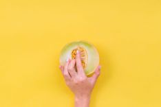 Frau, die ihre Finger in eine halbe Melone einführt