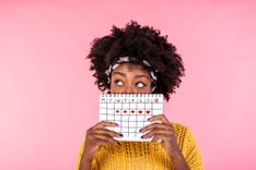 Frau hält sich einen Menstruationskalender vors Gesicht