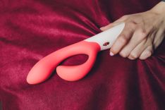 Dildo mit Sperma - Abbildung eines Vibrators auf einem roten Samttuch, gehalten von einer weiblichen Hand.