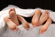 Bettdecke, unter der 3 Paar Füße hervorschauen