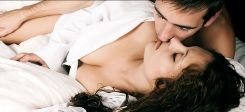 Paar liegt mit verschränkten Händen im Bett und küsst sich