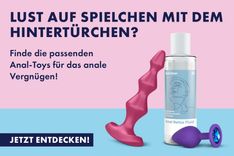 Roter Satisfyer Lolli-Plug 1 und lilaner Analplug mit blauem Stein, die gegen ein Satisfyer Anal Relax Fluid gelehnt sind vor rosa-blau geteiltem Hintergrund