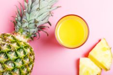 Ananas und ein Glas mit Ananassaft auf pinkem Hintergrund